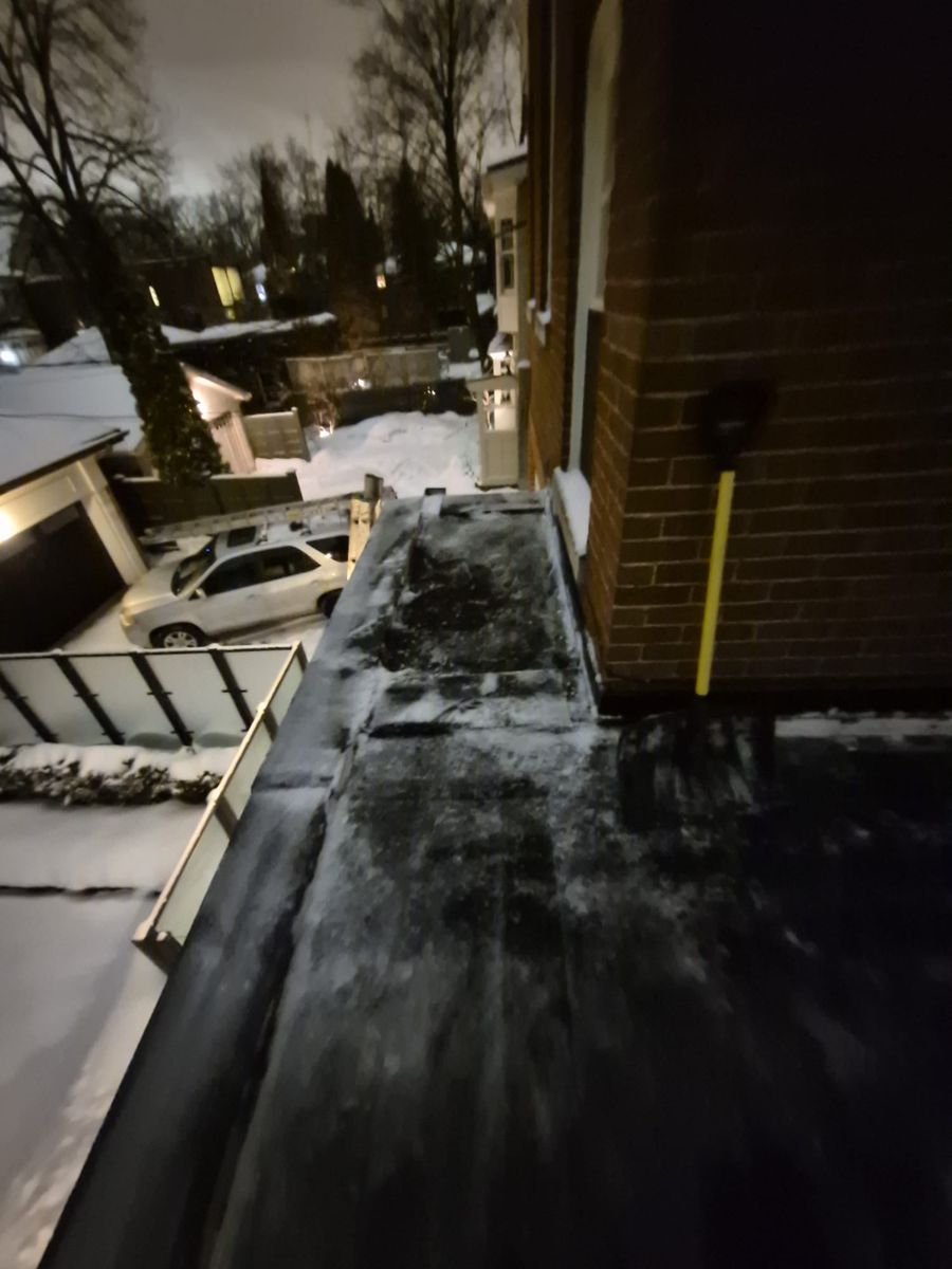 Snow shovel resting on a narrow roof ledge cleared beside a brick wall